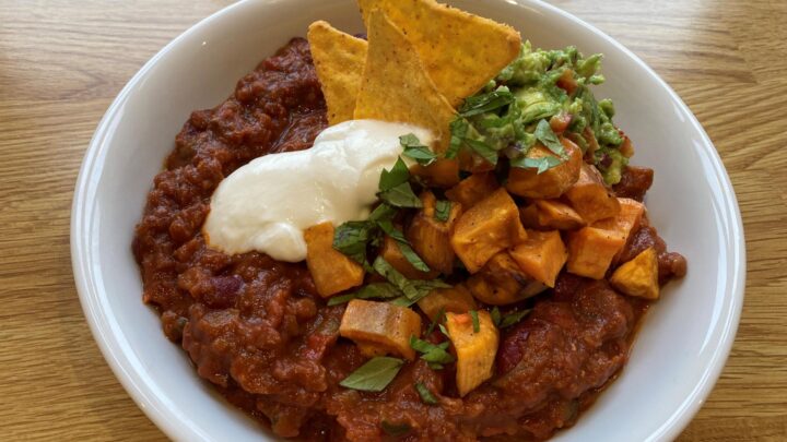 Chili sin carne serveret med tortillachips, cremefarice og hakket grønt i en hvid dyb tallerken.