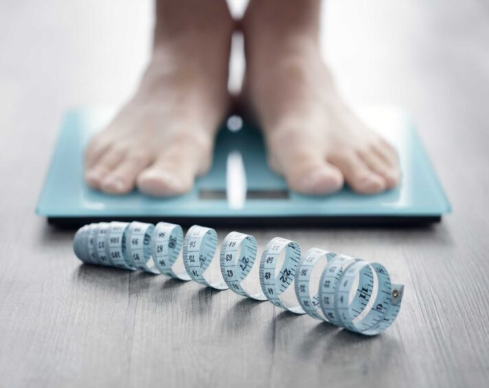 Person står på en vægt med et målebånd foran på gulvet