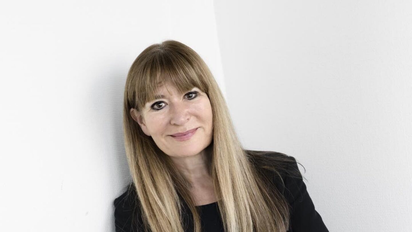 Bente Klarlund, professor - står foran hvid væg med hænderne over kors.