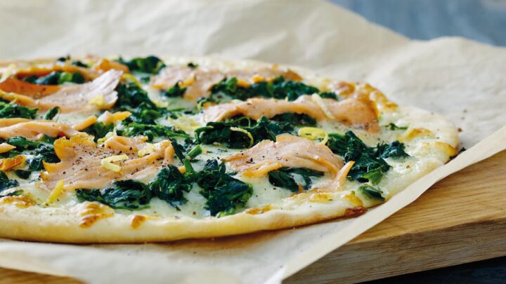 Tarte flabée med røget laks og spinat liggende på bagepapir og skærebræt af træ