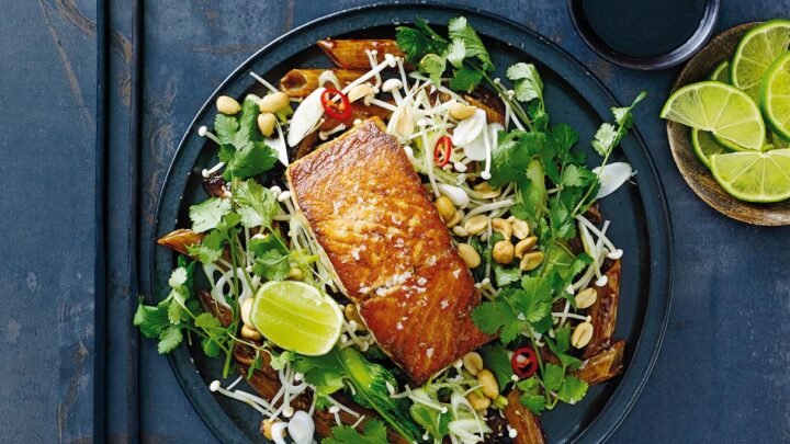 Stegt laks med wokket pak choi og pasta serveret på mørkeblå stentøjstallerken og med skiver af lime