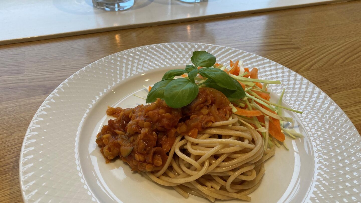 Linsebolognese med spaghetti og grønt serveret på en mønstret hvid tallerken.