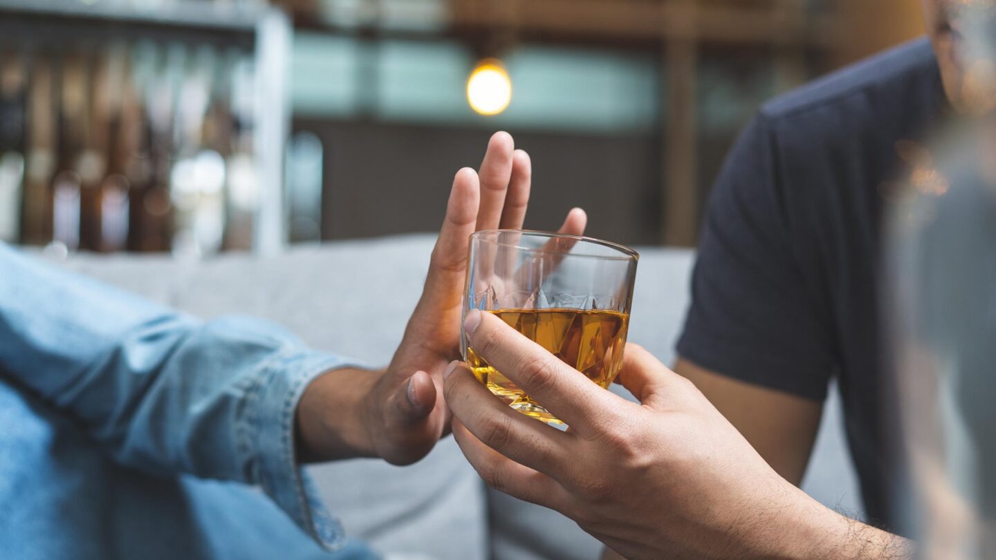 Person siger nej til alkohol ved at holde son ene hånd foran et glas, der tilbydes.