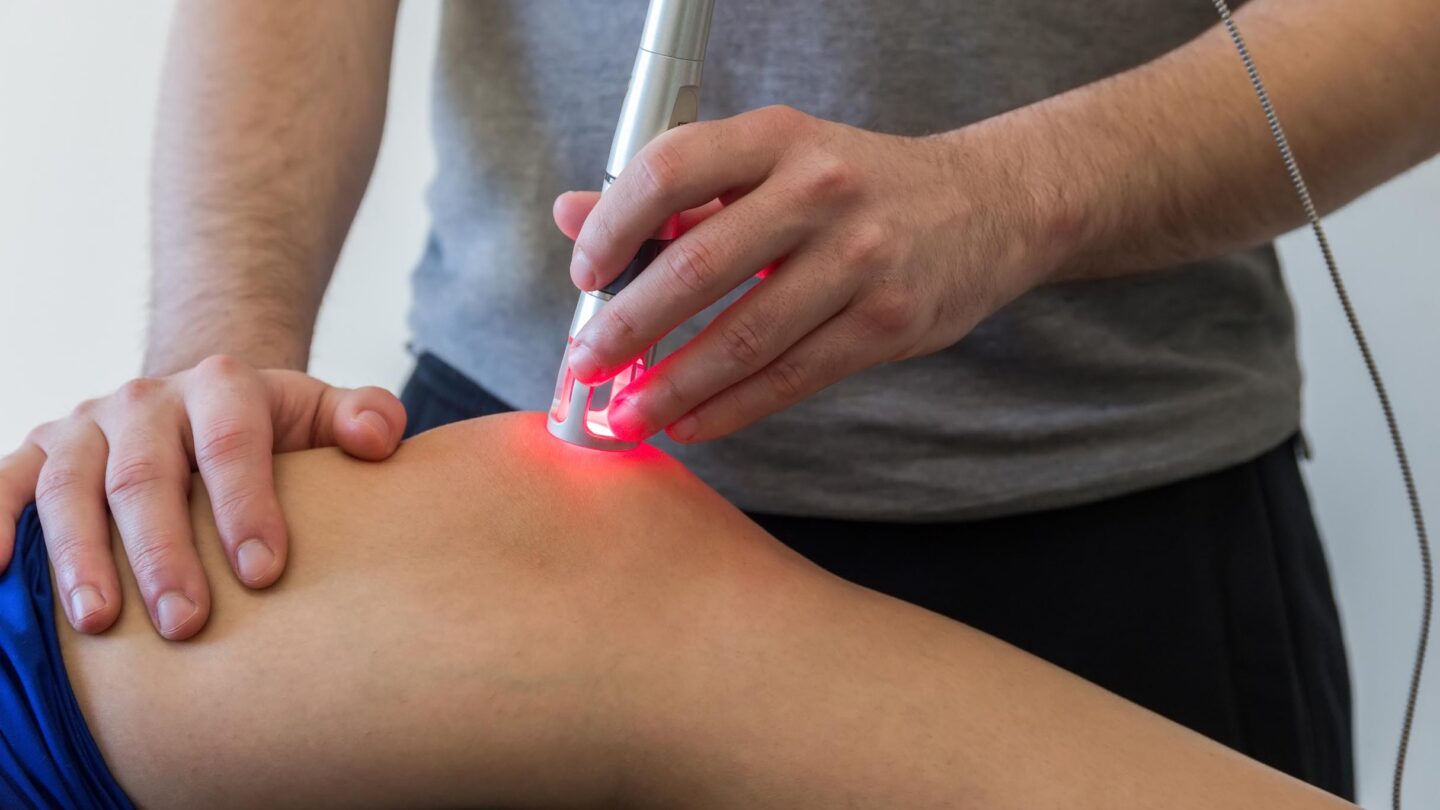 En behandler udfører laserterapi på en persons ene knæ.
