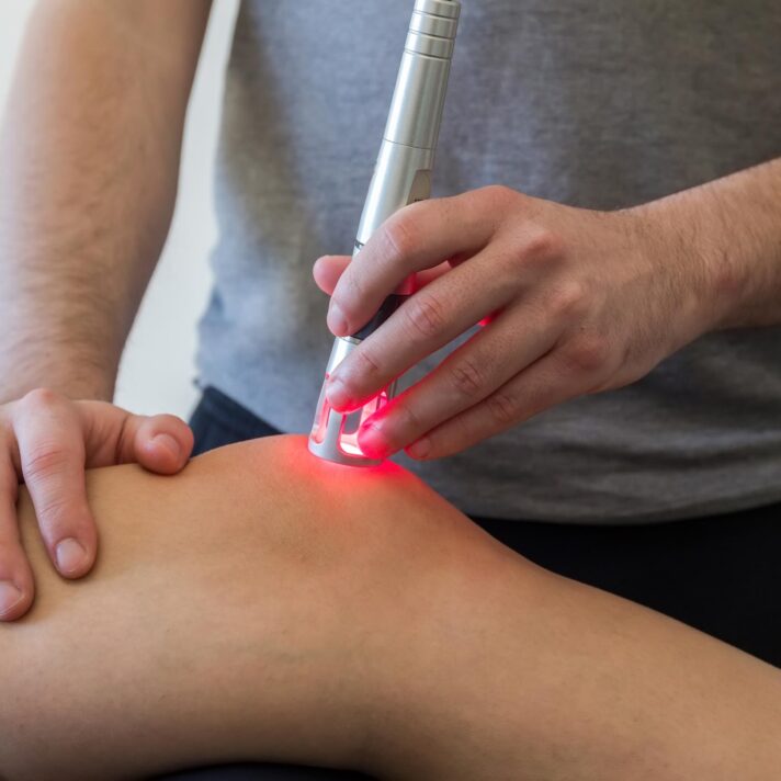 En behandler udfører laserterapi på en persons ene knæ.
