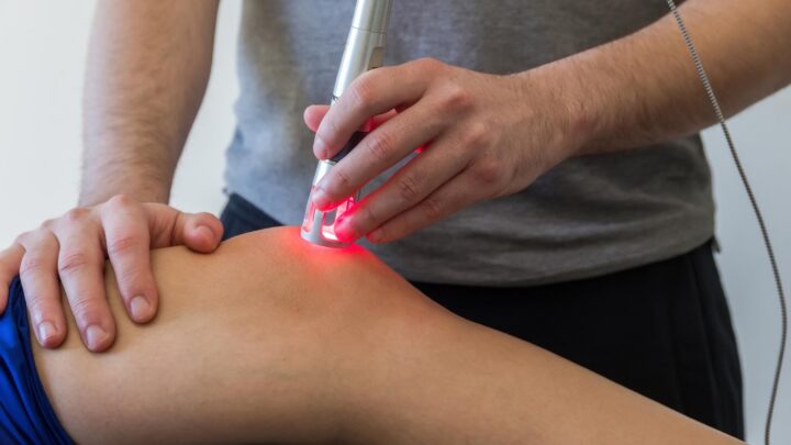 En behandler udfører laserterapi på en persons ene knæ.
